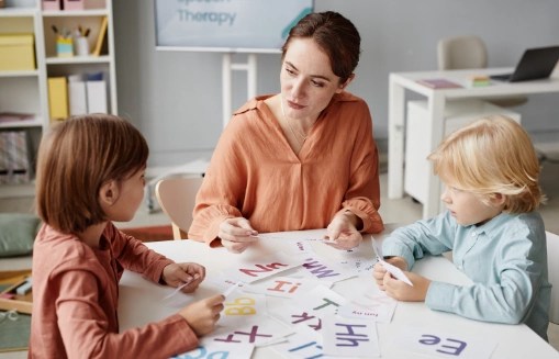 Logopedka pracuje z dwójką dzieci przy stoliku, na stole rozłożone karty z literami
